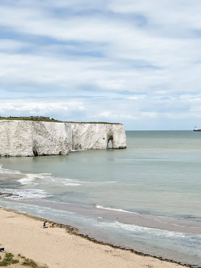 a beach with a large white cliff in the middle of the ocean.