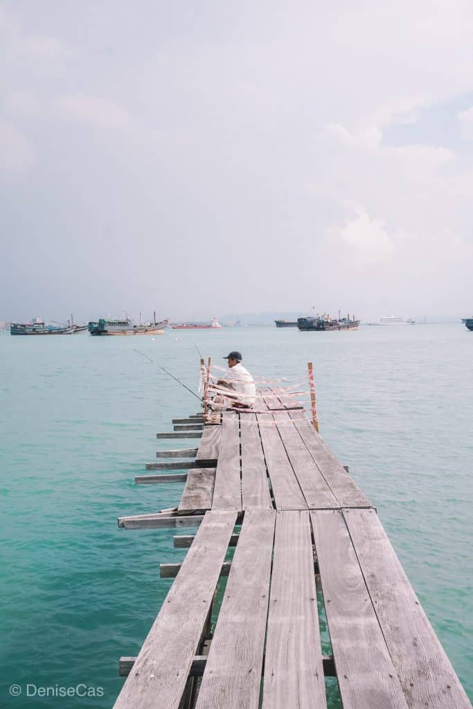 a man sitting on a dock fishing in the ocean.