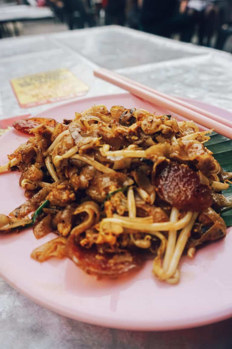 A Penang-style dish featuring a pink plate with noodles and meat.