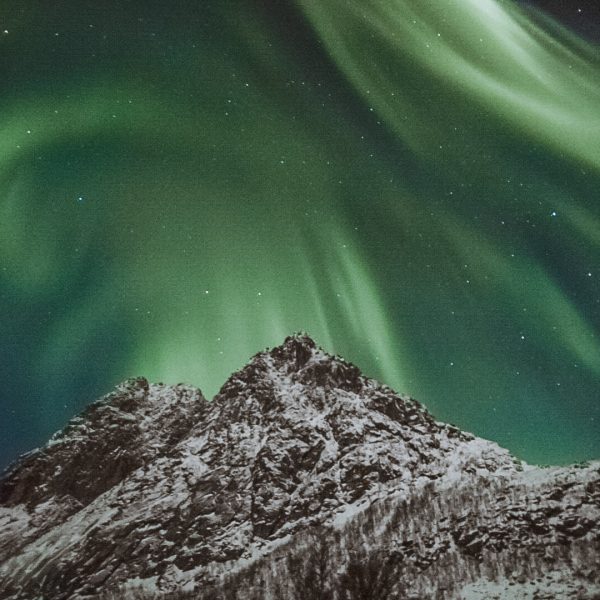 A Northern Lights display in Tromso, Norway over a snow-capped mountain.