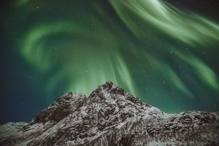 A Northern Lights display in Tromso, Norway over a snow-capped mountain.