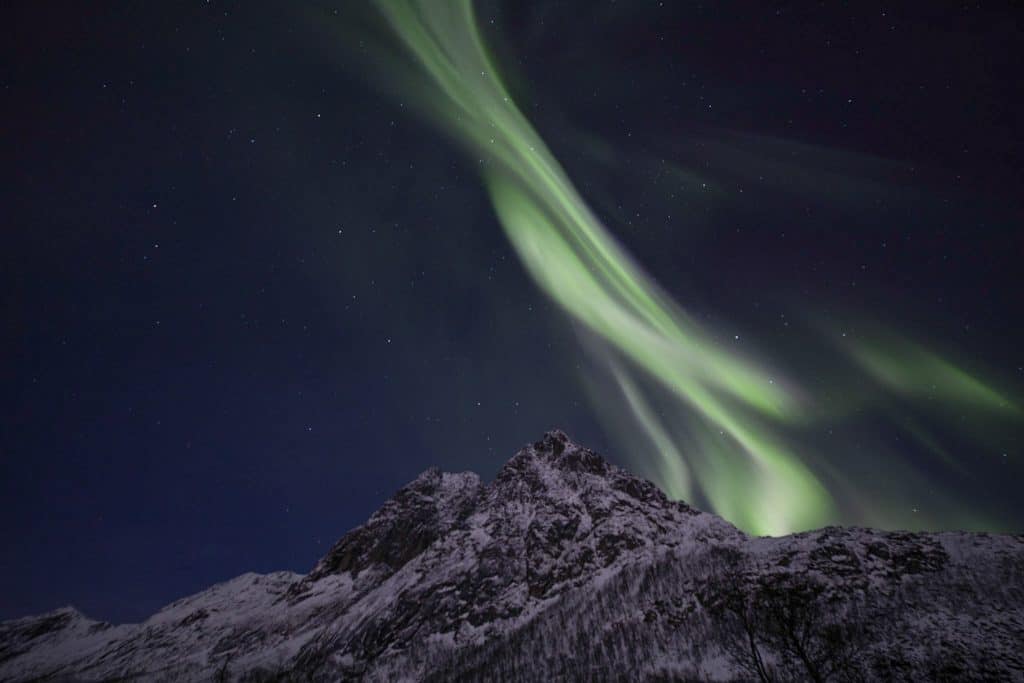 a green and white aurora bore above a snowy mountain.