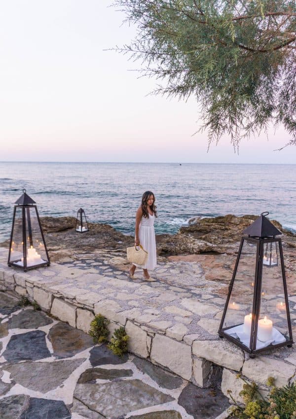 A woman standing on a stone walkway at a Crete resort next to a body of water.
