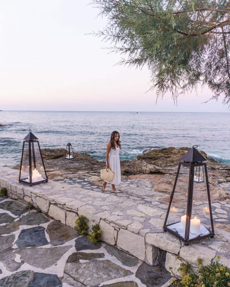 A woman standing on a stone walkway at a Crete resort next to a body of water.