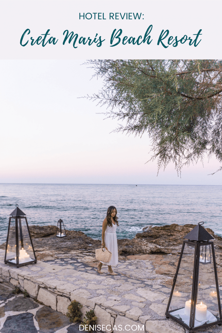 a woman in a white dress standing on a stone walkway next to the ocean in Crete, Greece.