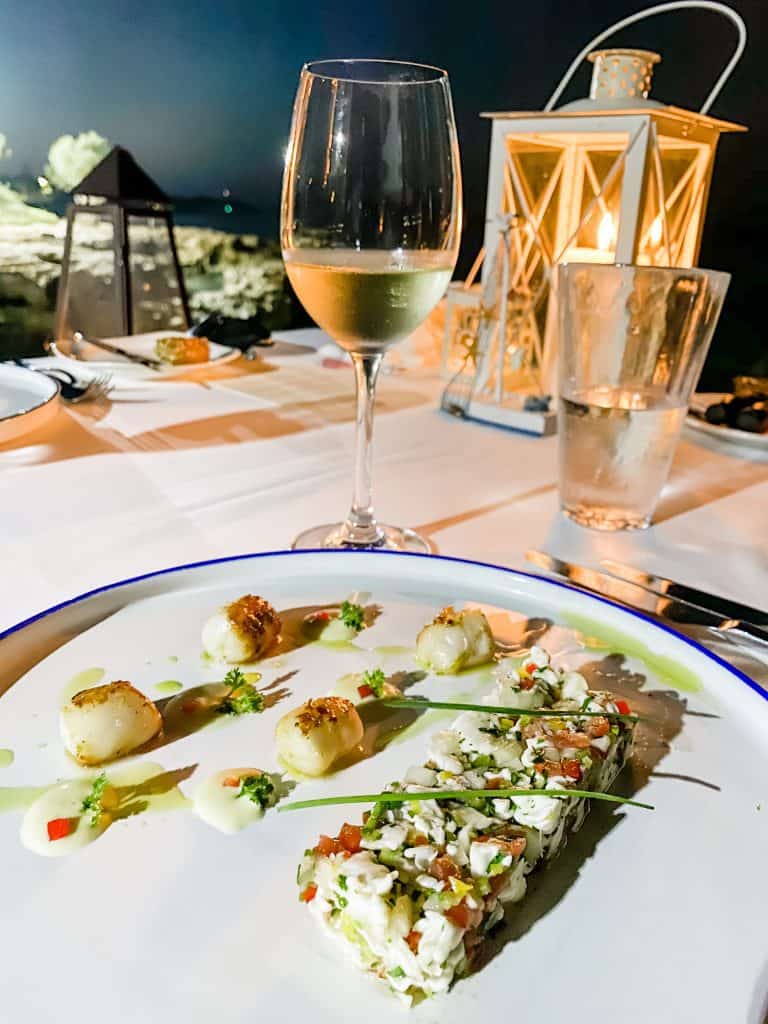 a white plate topped with food next to a glass of wine.
