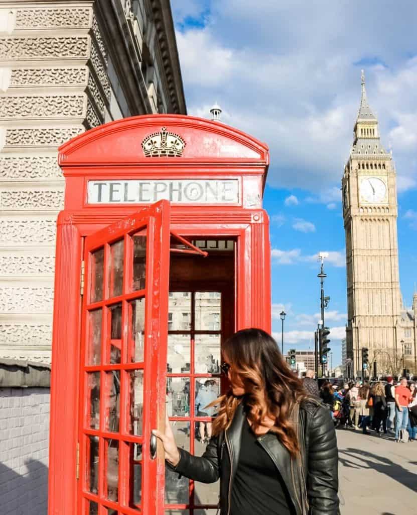 a woman standing next to a red phone booth.