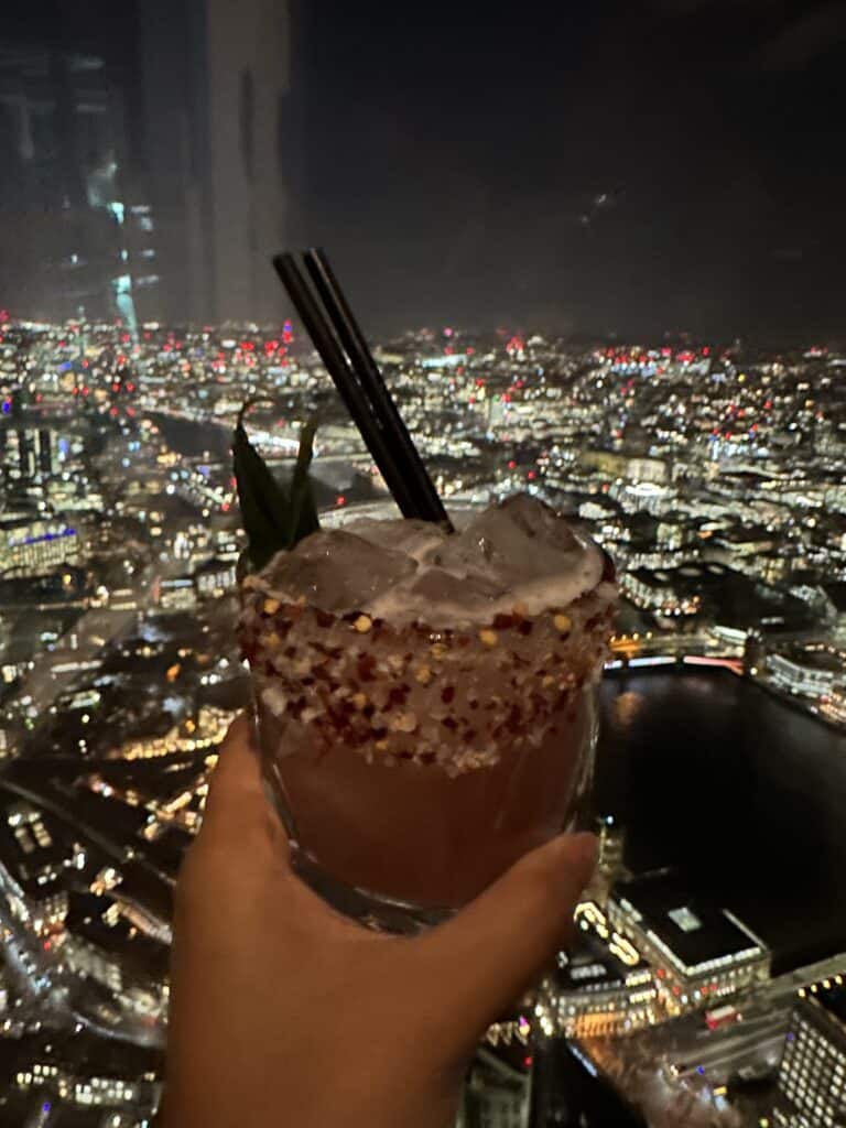 Is London Safe - A hand holding a cocktail in the View from the Shard Viewing Deck in London to show you to watch out for your drinks when on a night out in london for safety precaustions 